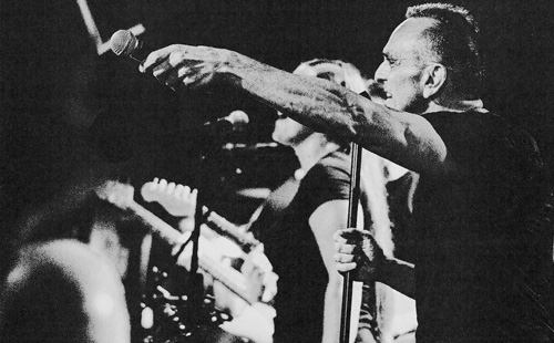 A black and white image of Hank Azaria singing with the band - arm outstretched with a microphone